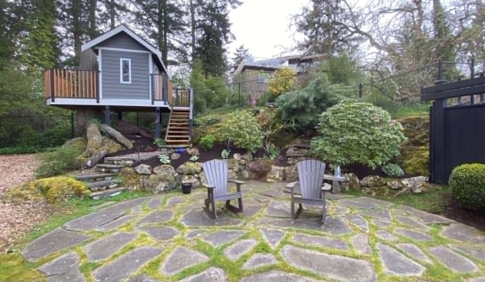 Manicured lawn and garden beds beside a treehouse and patio